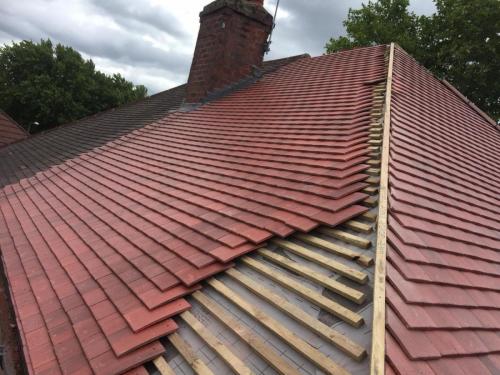 A half covered roof of red tiles showing some wooden struts underneath. This is a view of a partially complete job that is under progress at the time of the photo. Taken from roof level.