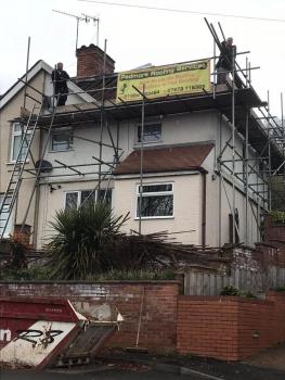 A ground level view of roofing work. Scaffolding surrounds the house