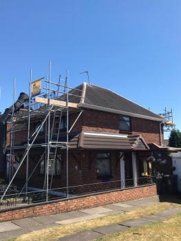 A ground level view of a roofing job. Scaffolding surrounds the house.