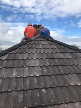 Two members of the team sitting on the apex of a house carrying out work on the property.