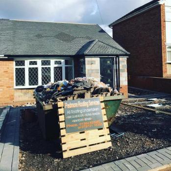 A property where roofing work. An advertising board displaying the service sits propped up against a skip used for the job.