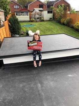 Pedmore Roofing Services sign being held by a girl while sat on a flat roof
